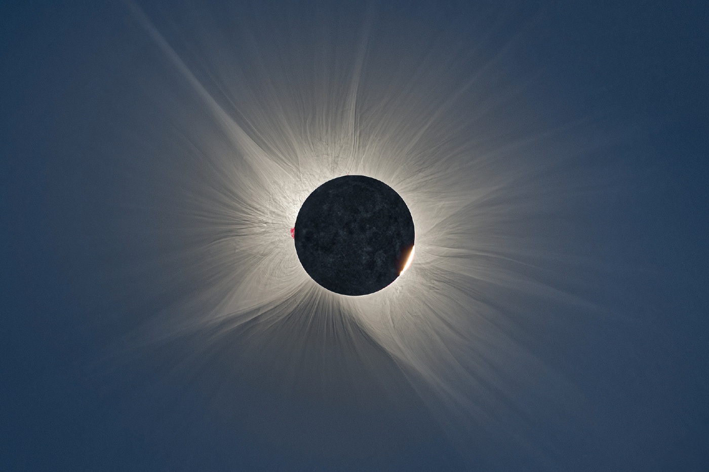 Total solar eclipse corona, 2026, photographed from Burgos in Spain, with a red prominence on the left of the lunar limb and a bright bead of photosphere at its lower right.